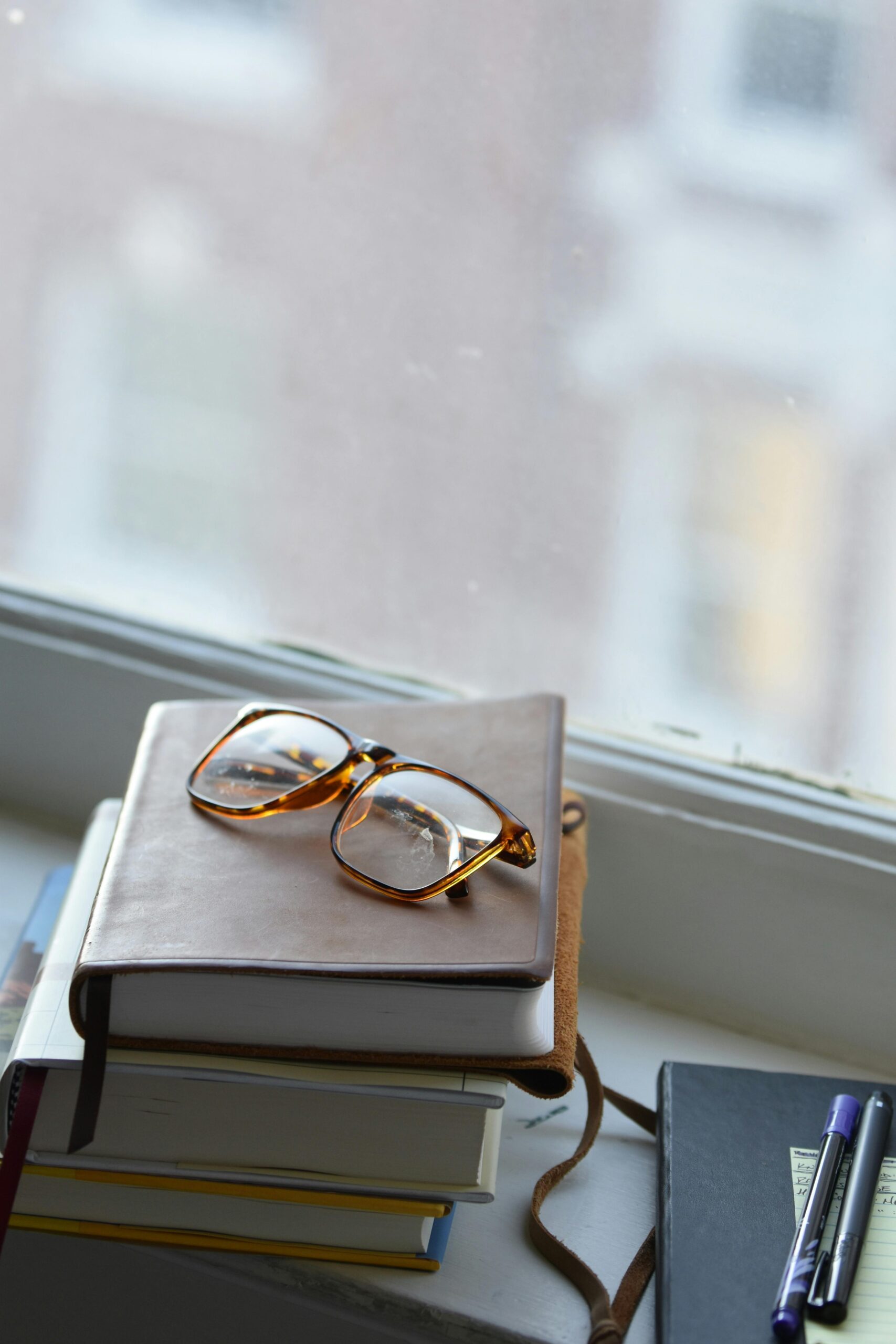 A cozy scene with eyeglasses on a notebook, stacked with books by a window in Memphis.